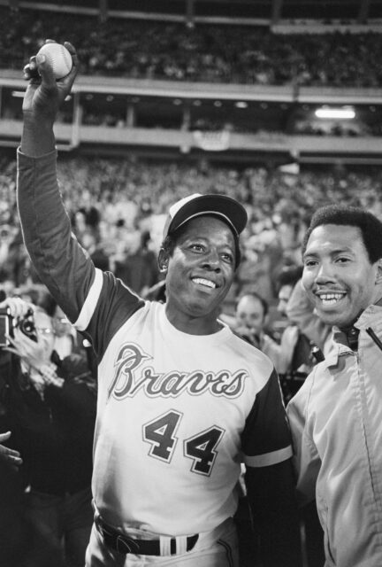 Hank Aaron surrounded by fans holding up a baseball.