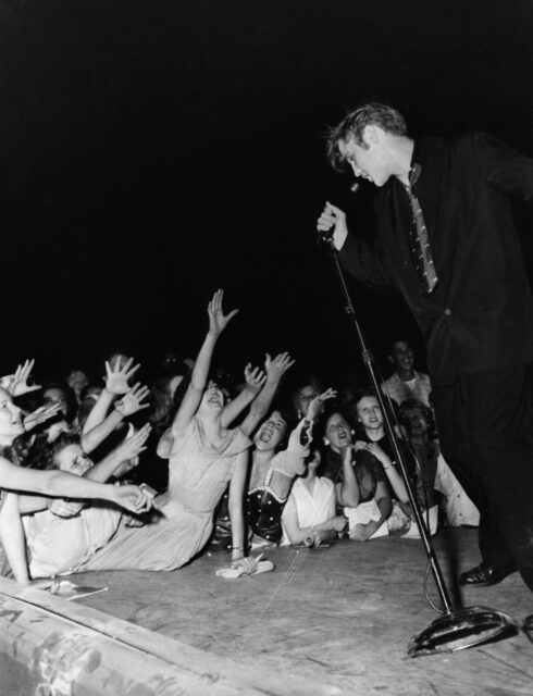 Elvis performing as girls reach up to him.