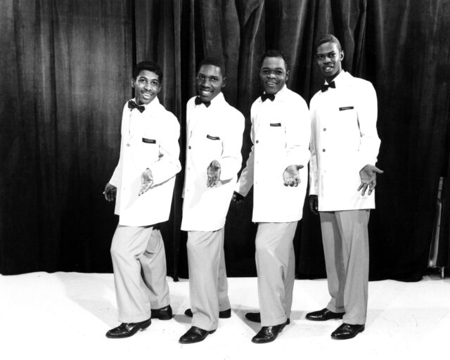 Four members of a doo-wop group in white suits.
