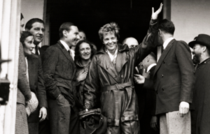 Amelia Earhart surrounded by people as she waves.