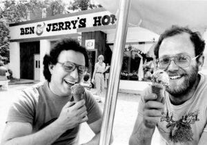 jerry greenfield and ben cohen smiling with ice cream cones outside of first ben and jerrys ice cream shop