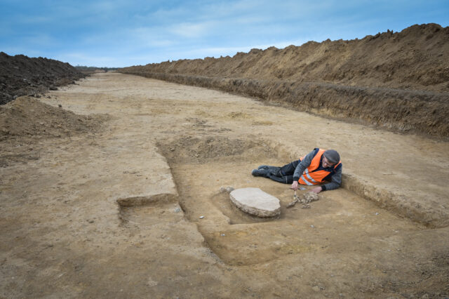 A man laying beside buried bones and a stone slab.