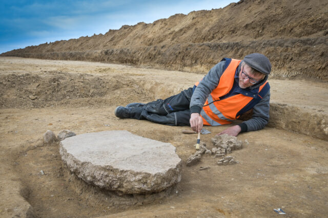 A man laying beside buried bones and a stone slab.