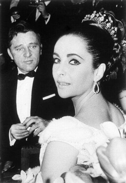 Elizabeth Taylor looks at the camera while Richard Burton looks at her.