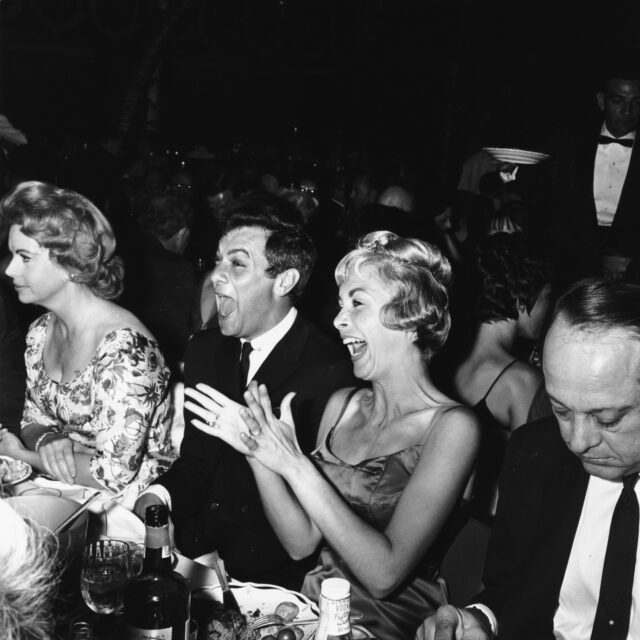 Tony Curtis and Janet Leigh sitting together and laughing.
