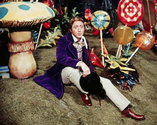 Gene Wilder as Willy Wonka sitting on the ground with lollipops standing around him.