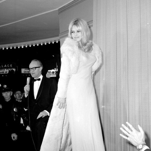 A man stands behind Brigette Bardot while she is on stage.