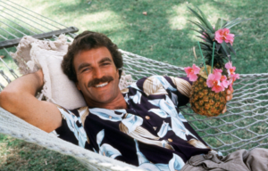 Tom Selleck laying in a hammock holding a pineapple.